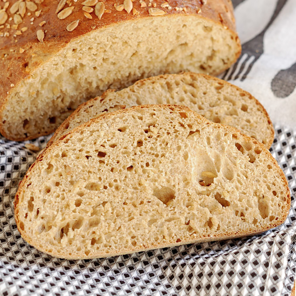 a sliced loaf of cracked wheat bread on a black and white towel.