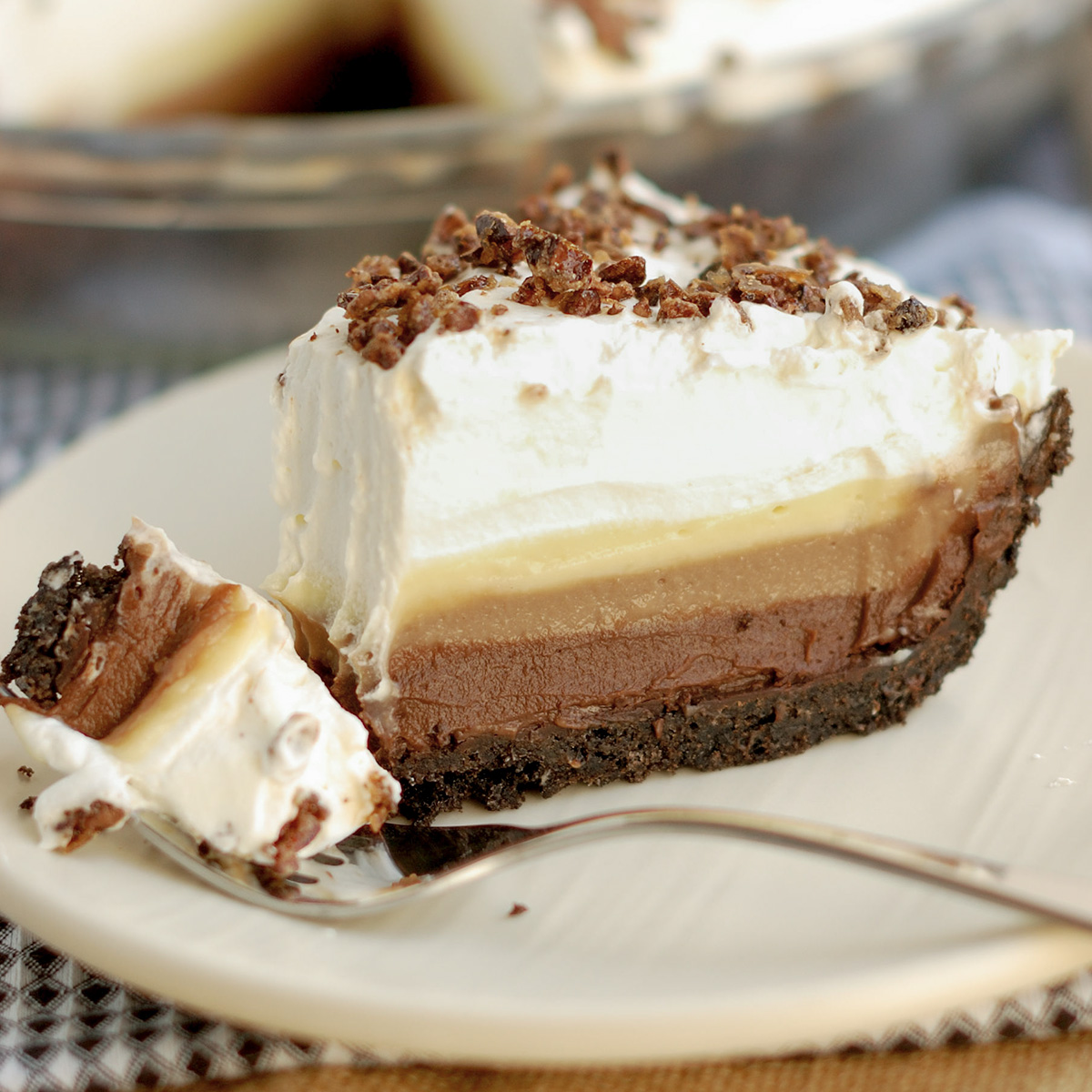 a slice of triple chocolate cream pie on a white plate with a spoon.