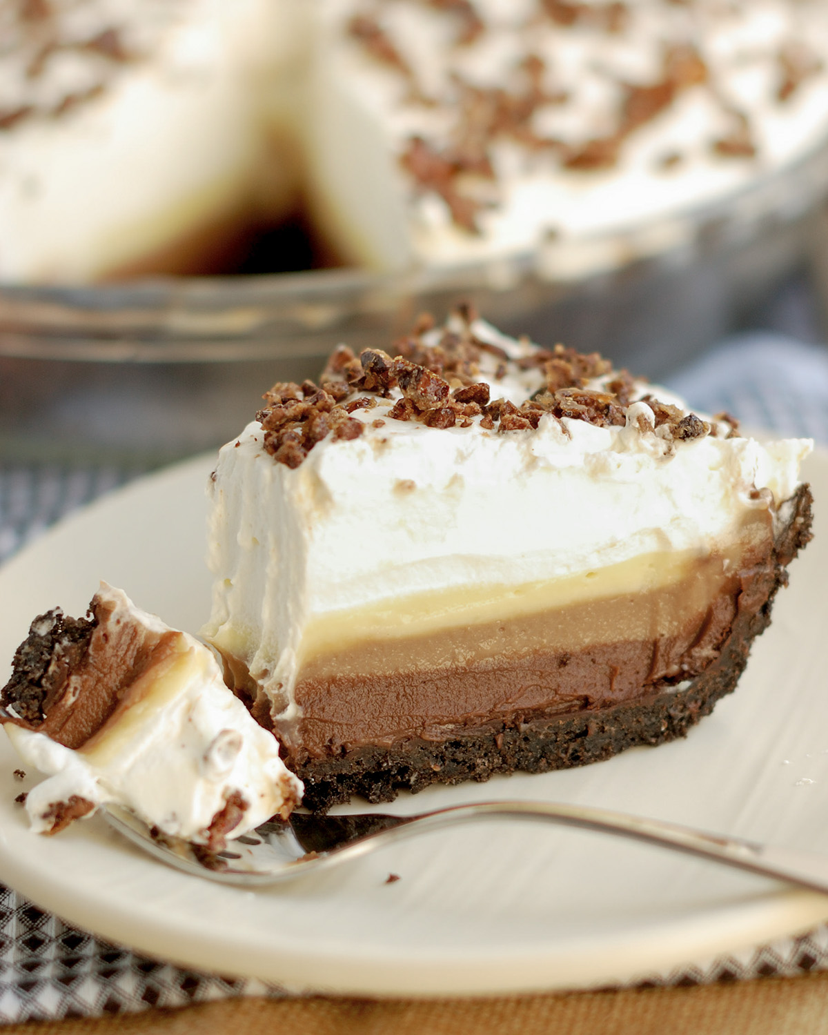 a slice of tripe chocolate cream pie on a white plate with a fork.