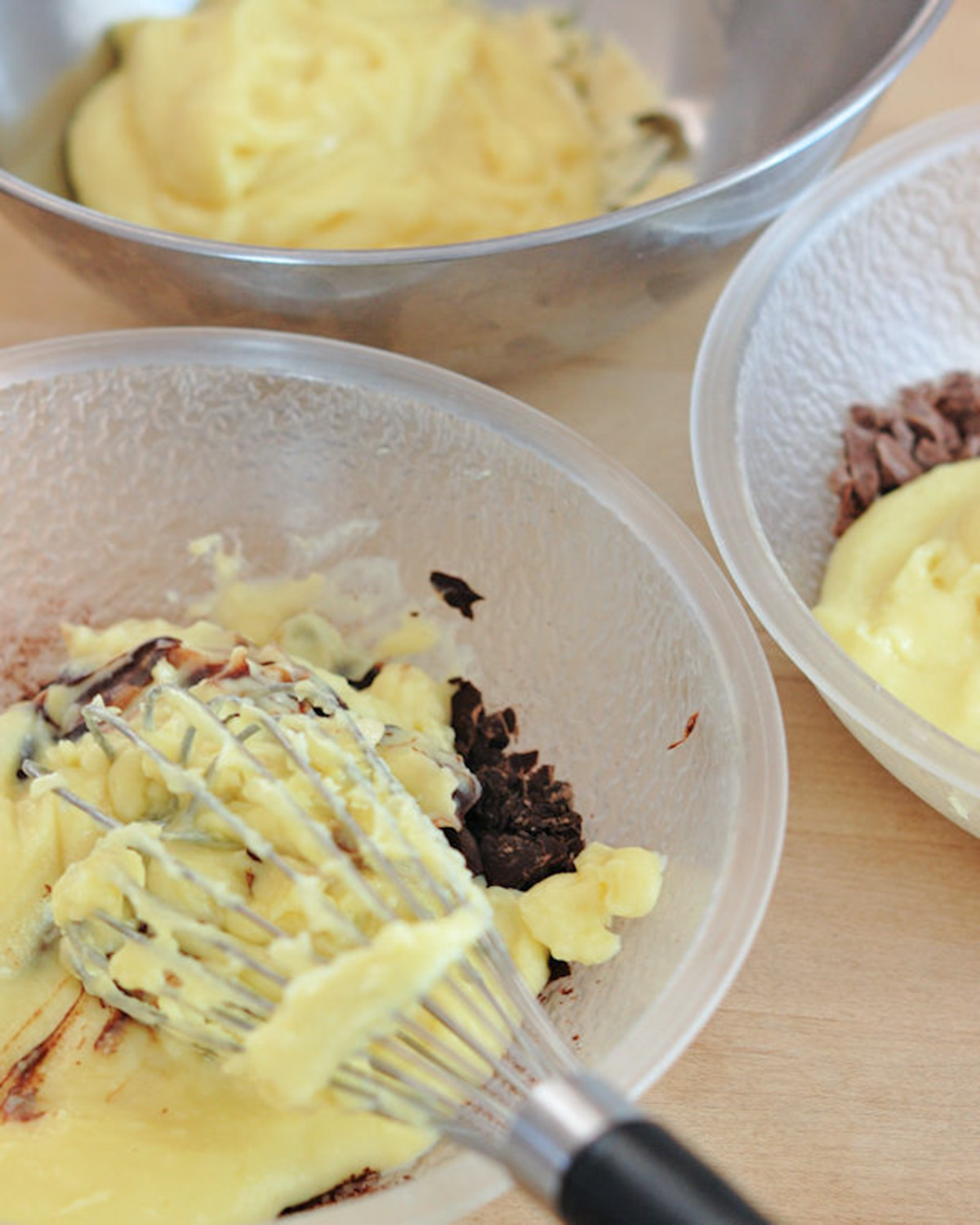 three bowl of pastry cream with white, milk and dark chocolate with a whisk.