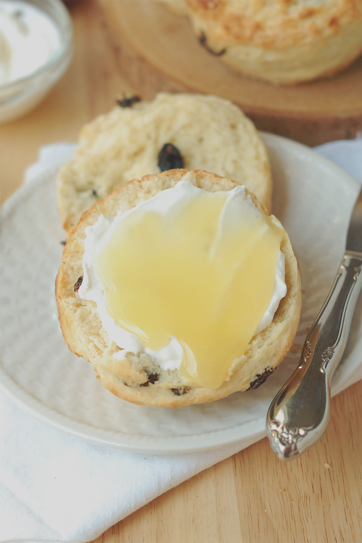 a scone with cream on lemon curd on a white plate.