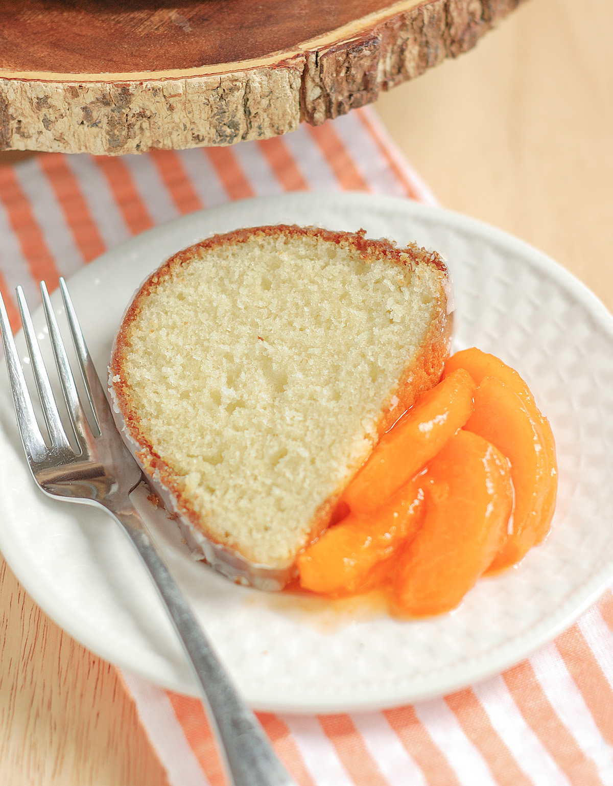 a slice of buttermilk bundt cake on a white plate with peaches.