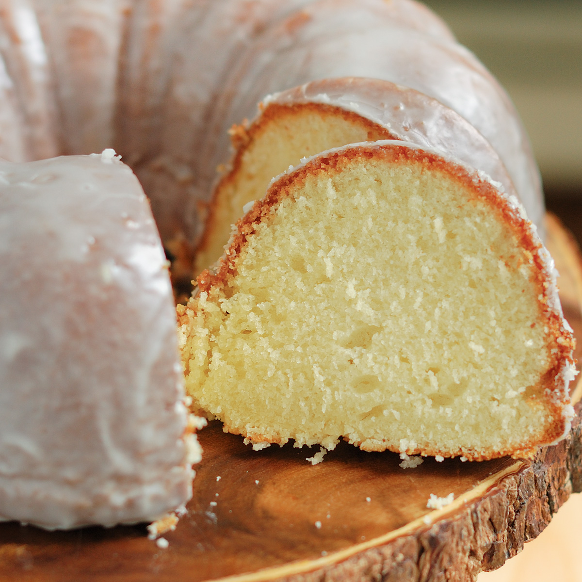 a sliced buttermilk glazed bundt cake on a wooden cake stand.