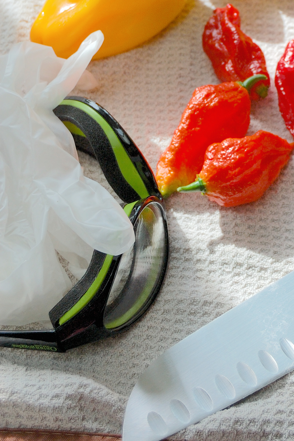 peppers, goggles, gloves and a knife on a towel.