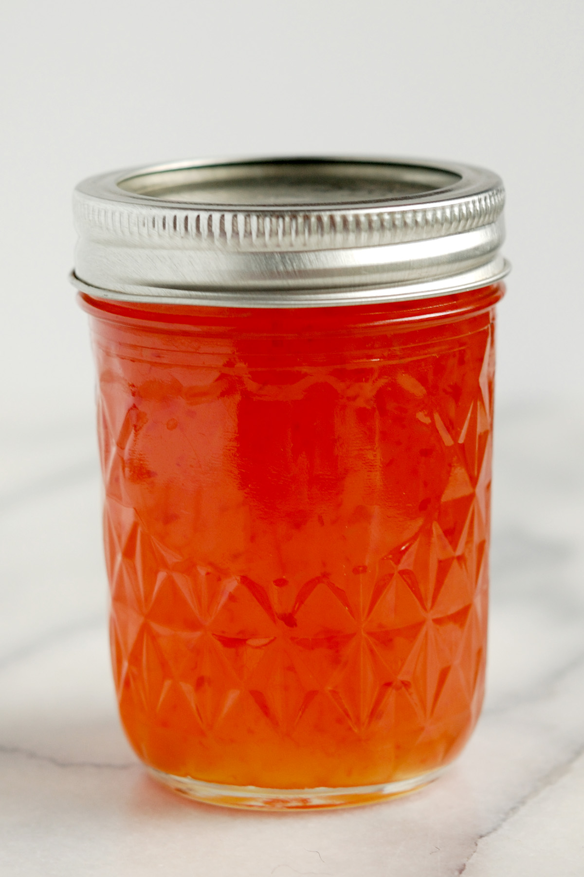 a jar of red pepper jelly on a white surface.