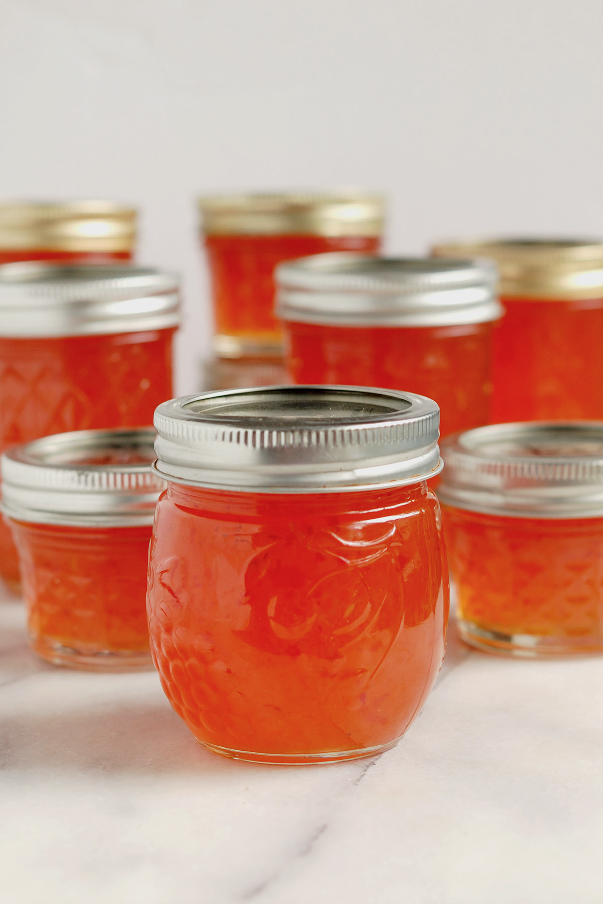 jars of red hot pepper jelly on a marble table.