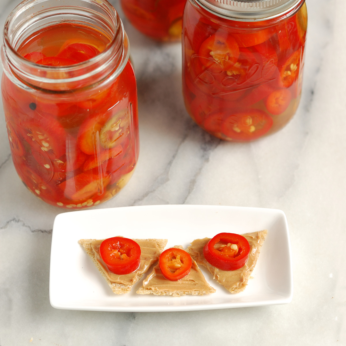 jars of pickled peppers and crackers with peanut butter and pickles on a white plate.