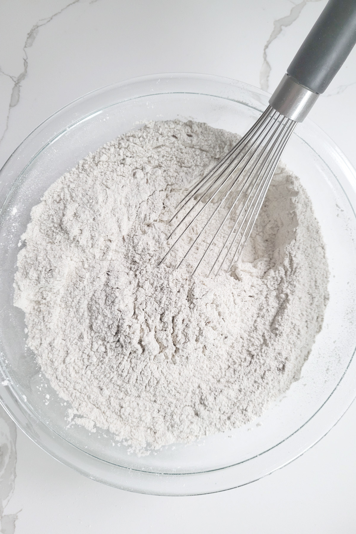 A glass bowl fill with flour with a whisk.