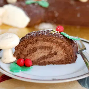 a slice of chocolate yule log cake on a white plate with meringue mushroom.s