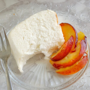 a slice of angel food cake with peaches on a glass plate with a fork.