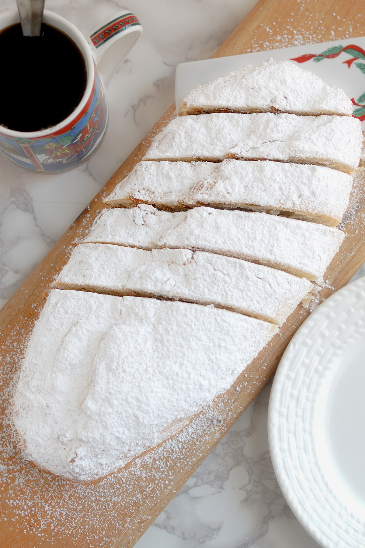 a sliced almond stollen on a wooden cutting board next to a cup of coffee.