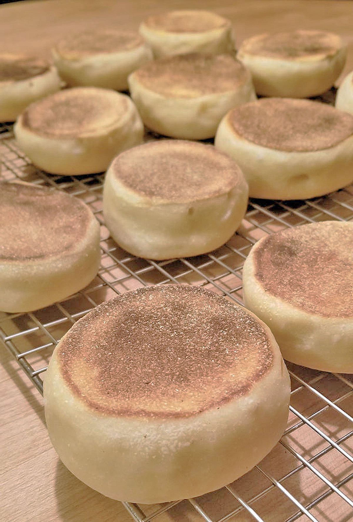 sourdough english muffins cooling on a rack.