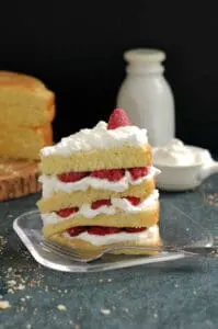 a slice of vanilla cake with raspberries and cream on a plate