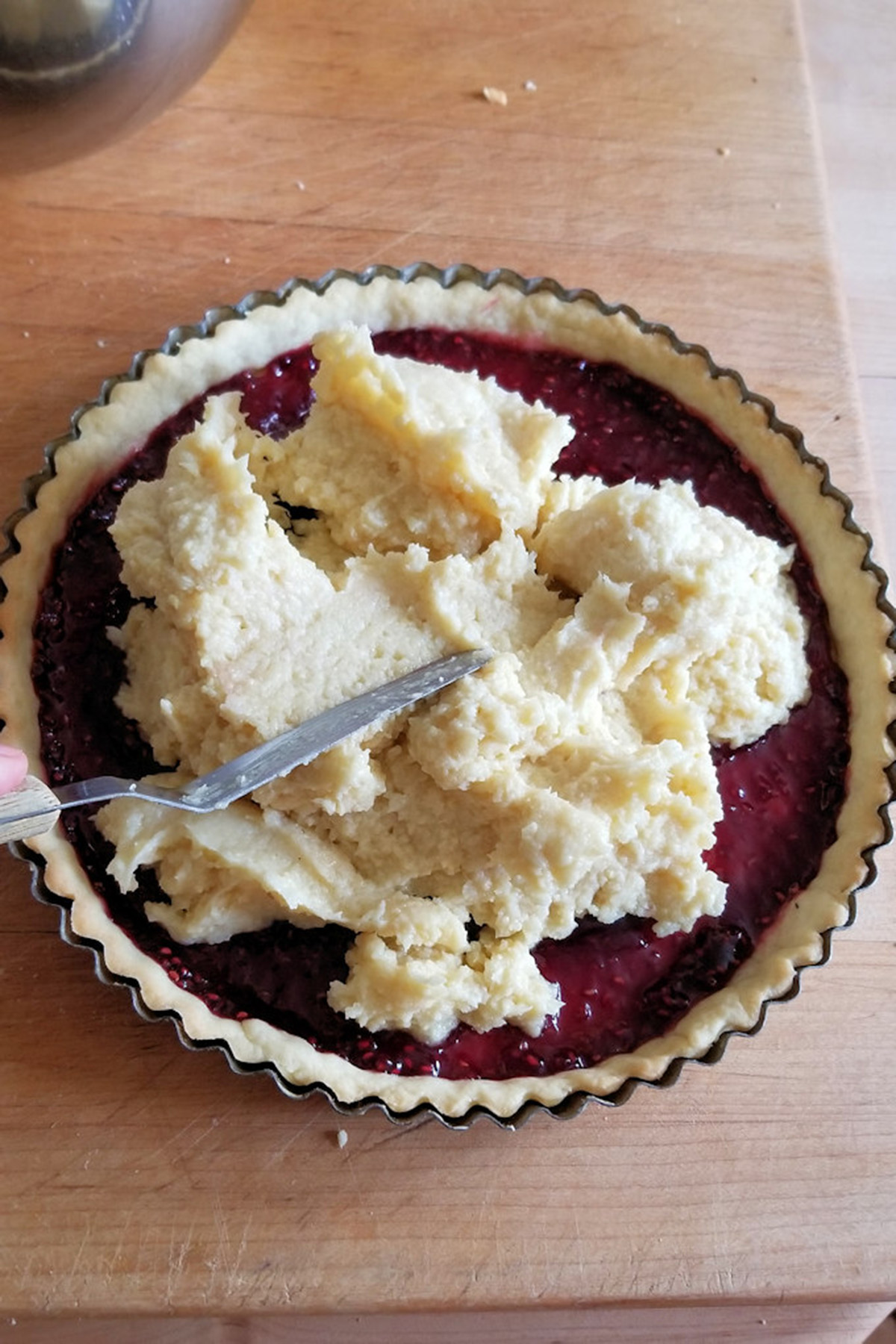 a tart pan lined with dough and filled with rapsberry preserves and almond paste.