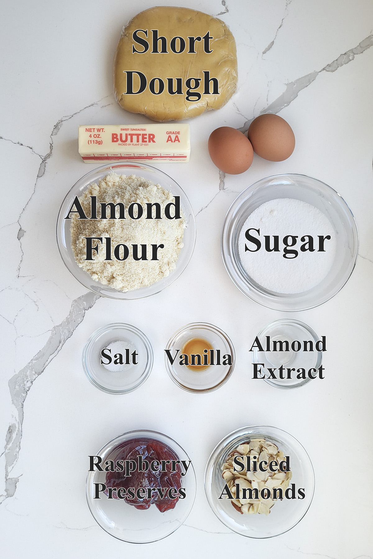 ingredients for bakewell tart in glass bowls on a white surface.