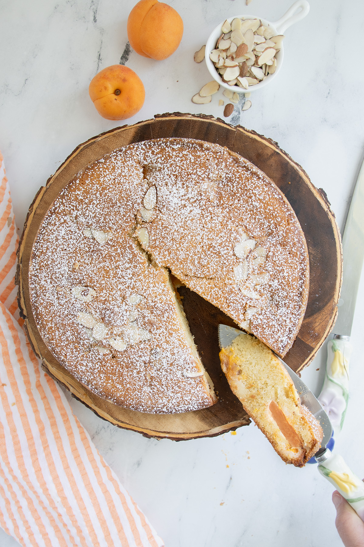 an apricot cake on a wooden cake stand with a slice removed.