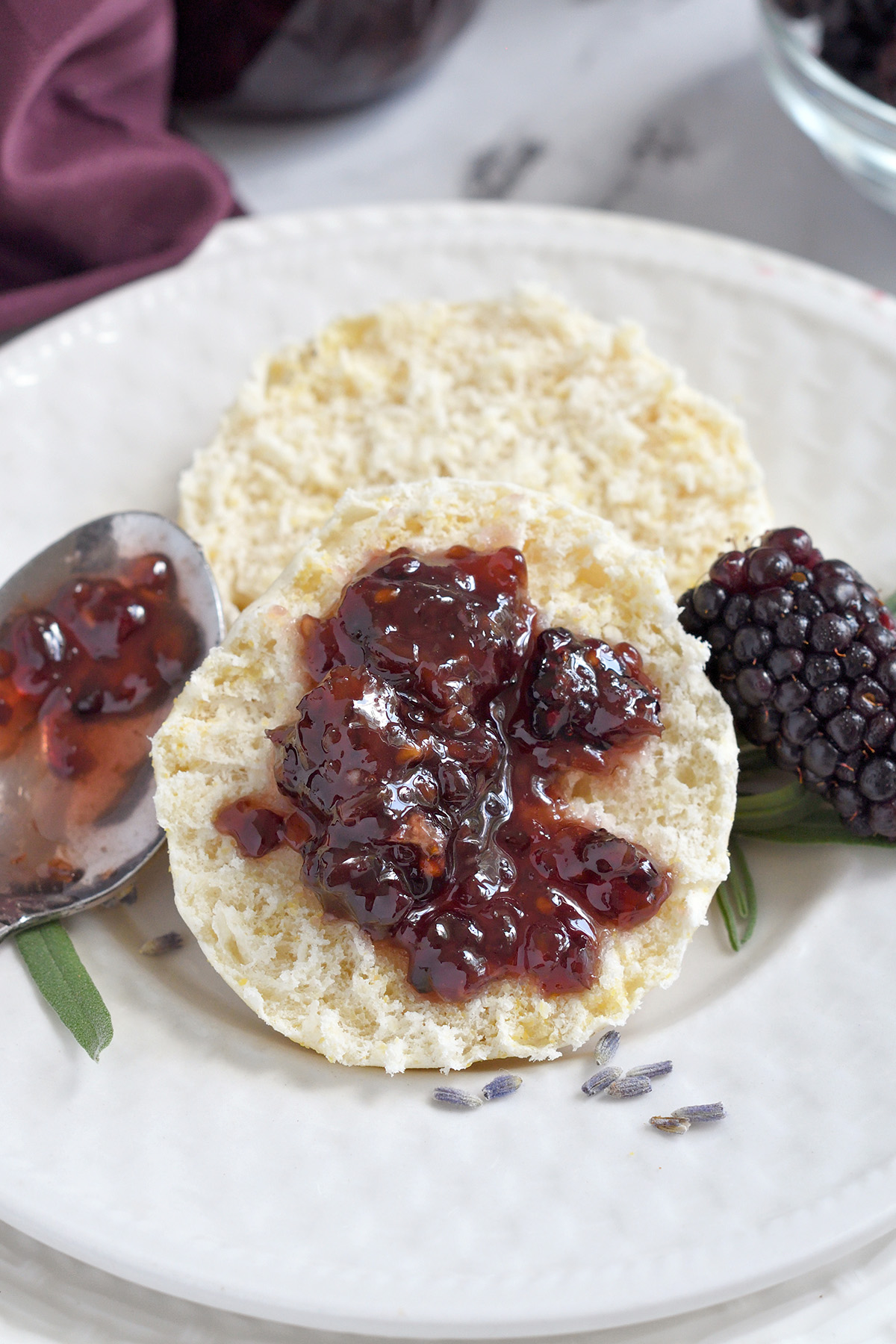 blackberry preserves on an english muffin on a white plate.