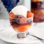 a glass bowl filled with ice cream and rumtopf fruit.