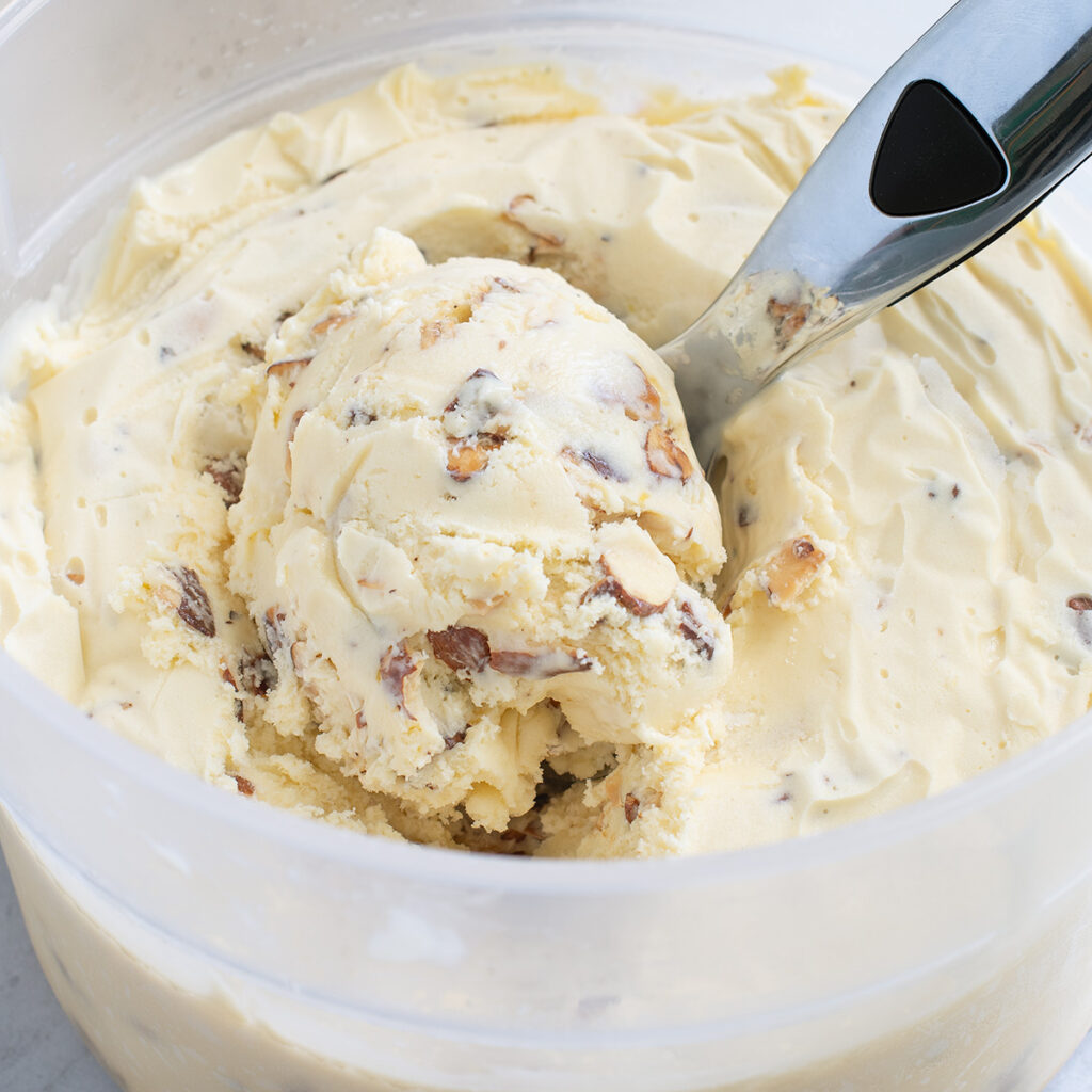a bucket of almond ice cream with a scooper.