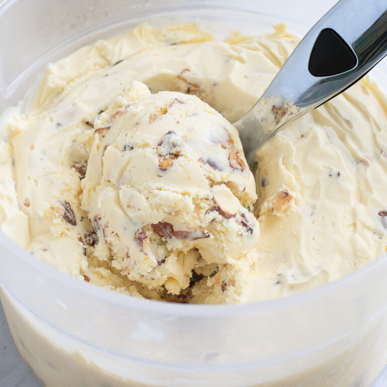 a bucket of almond ice cream with a scooper.