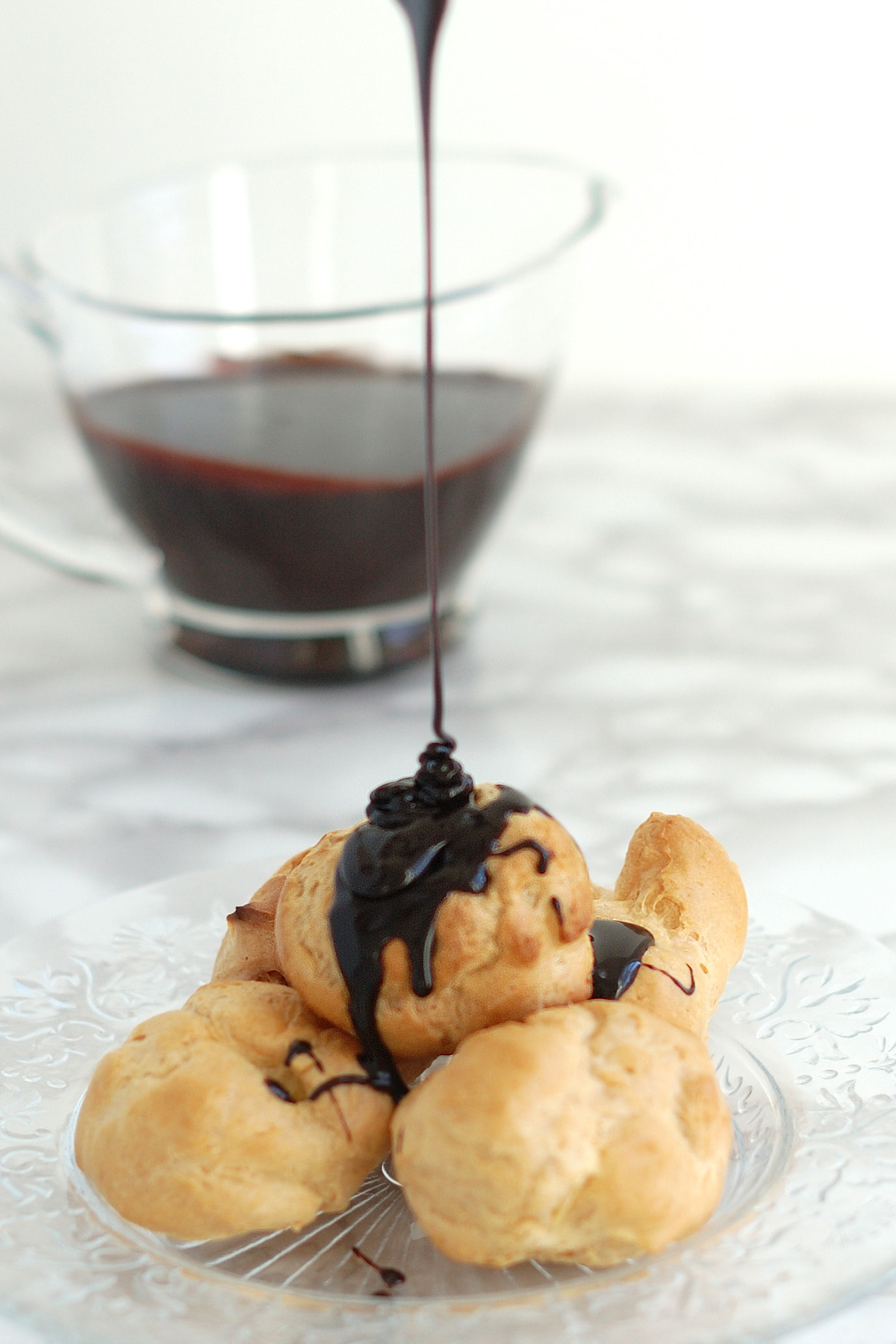 profiteroles on a glass plate drizzled with port wine hot fudge sauce.