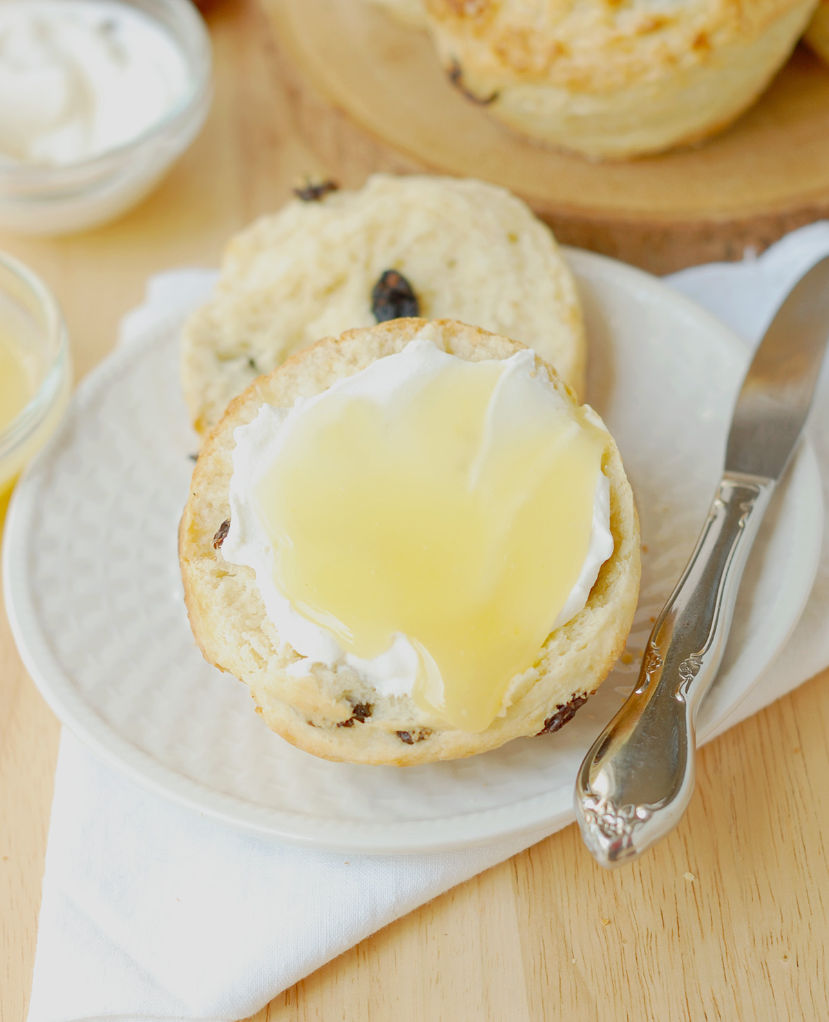 a scone with cream and lemon curd on a white plate.