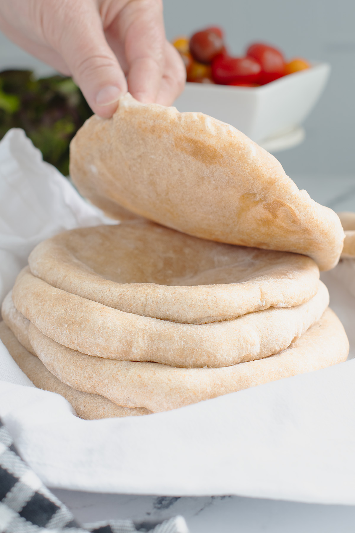 a hand lifting a pita bread off a stack set on a white cloth.