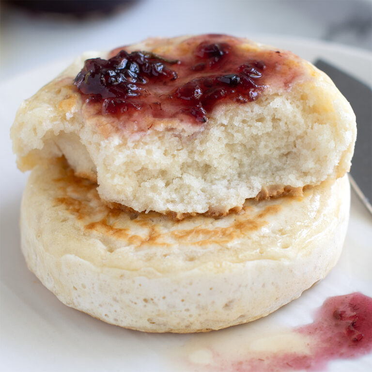 a jam topped crumpet on a white plate.