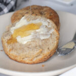 a rye scone with butter and honey on a white plate.