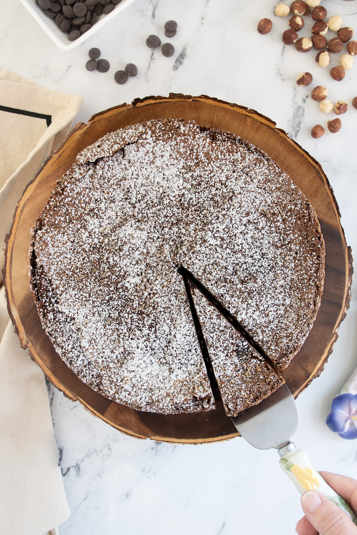 a chocolate hazelnut cake on a wooden cake stand with a slice cut.