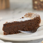 a slice of chocolate hazelnut cake on a white plate with a fork.