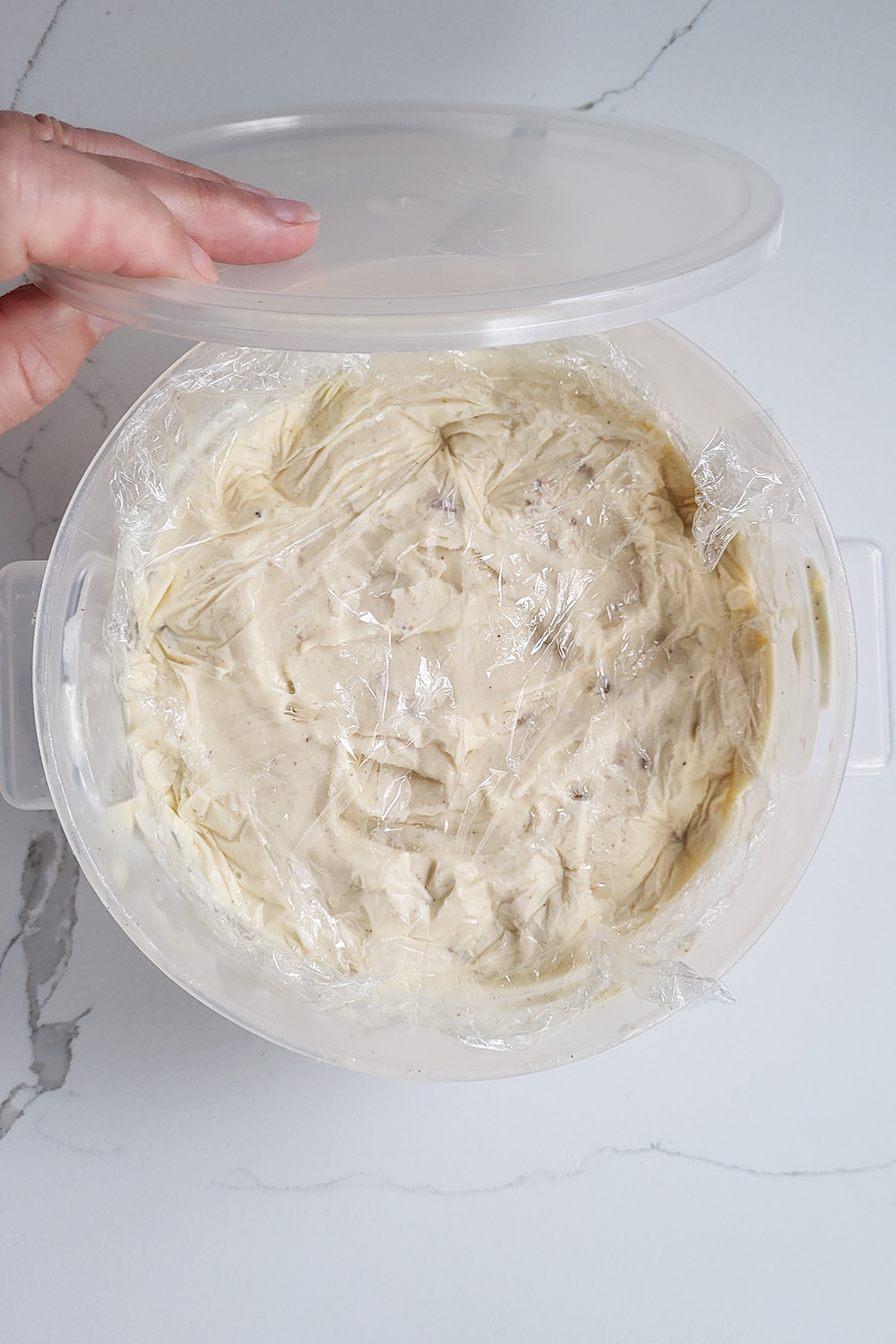 hazelnut ice cream with a layer of plastic wrap on top in a plastic container.