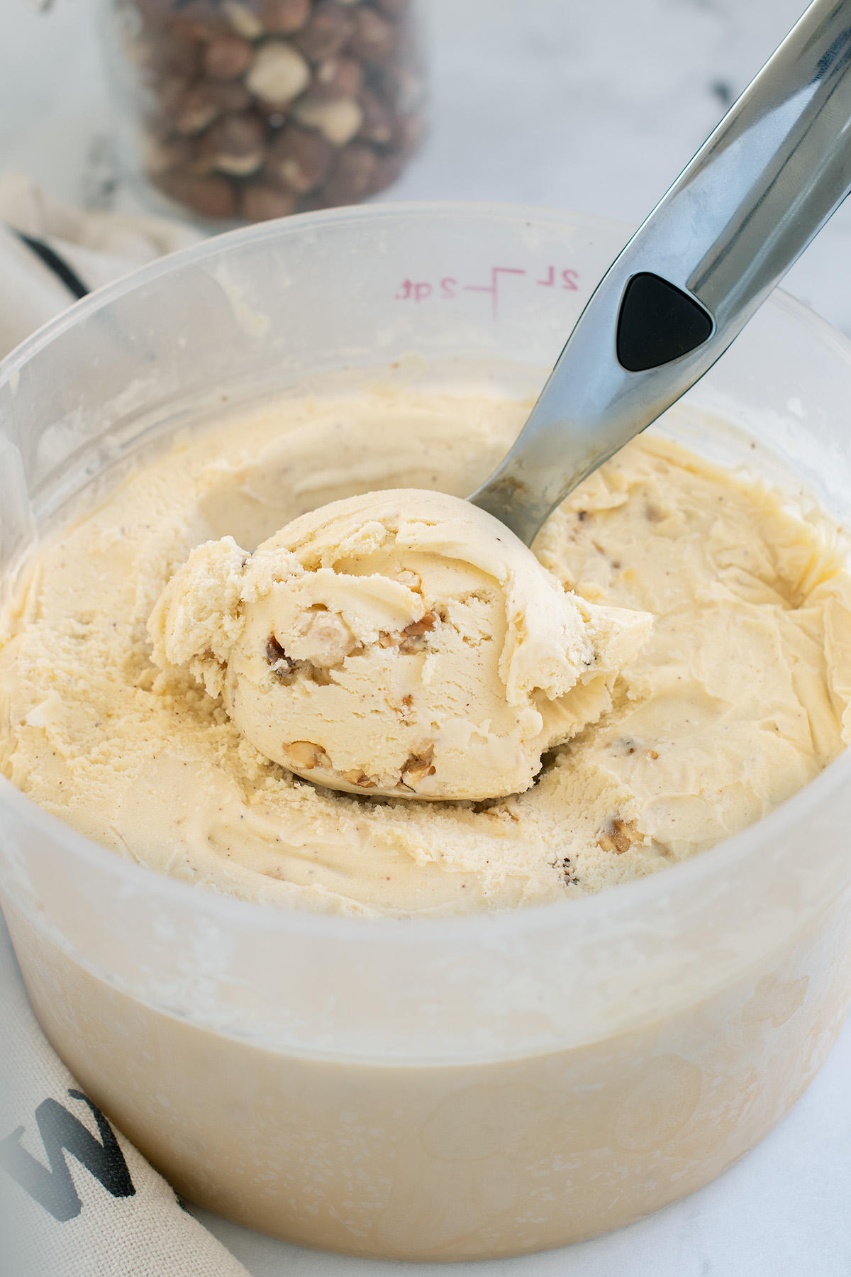 a plastic container full of hazelnut ice cream with an ice cream scoop.