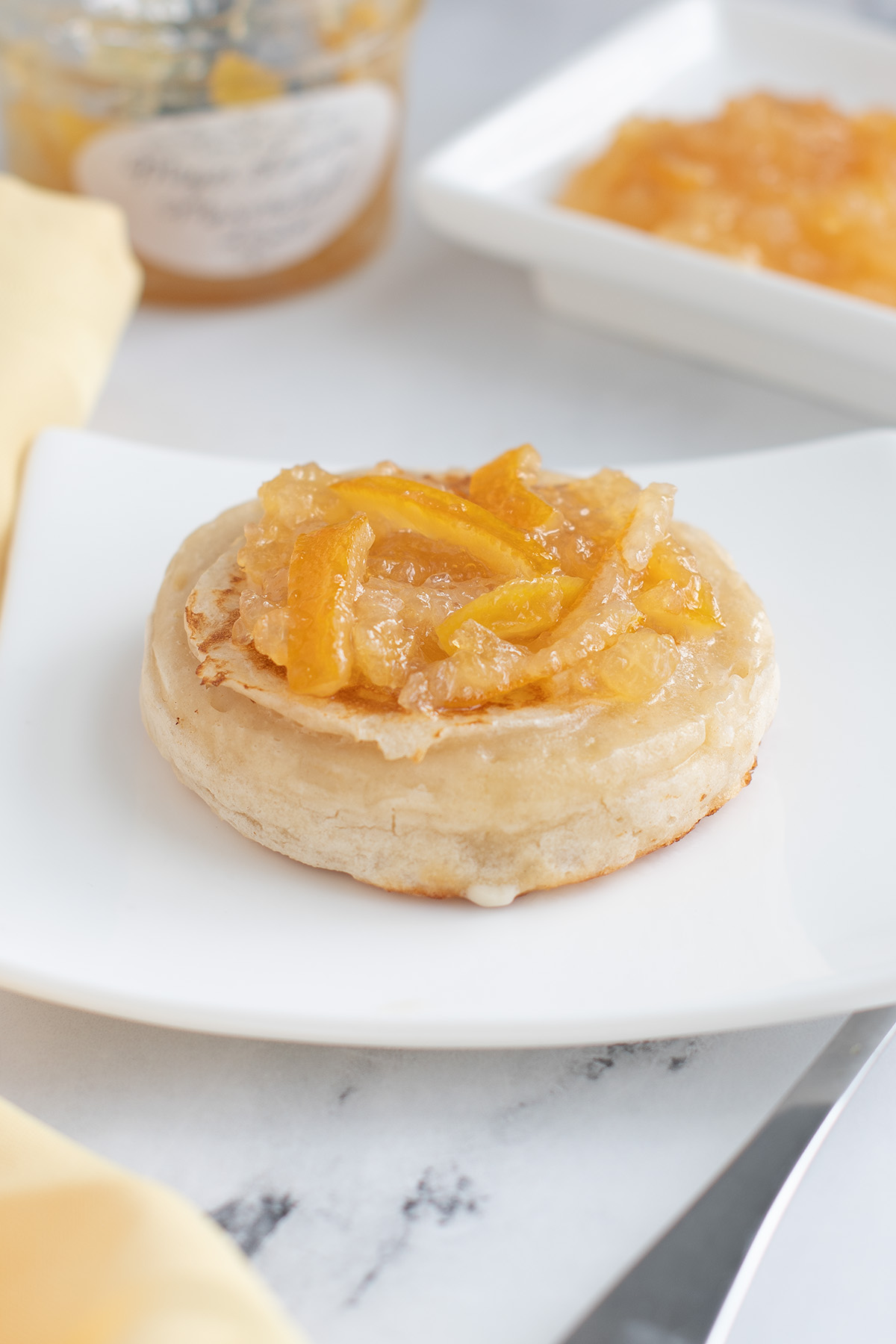 a crumpet on a white plate topped with meyer lemon marmalade.