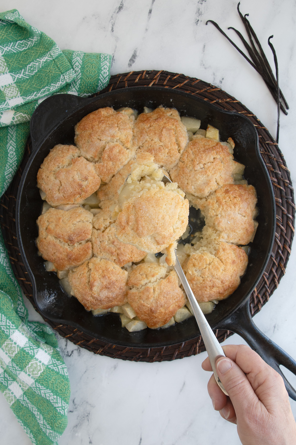 a pear cobbler in a cast iron skillet on a table with a green cloth.