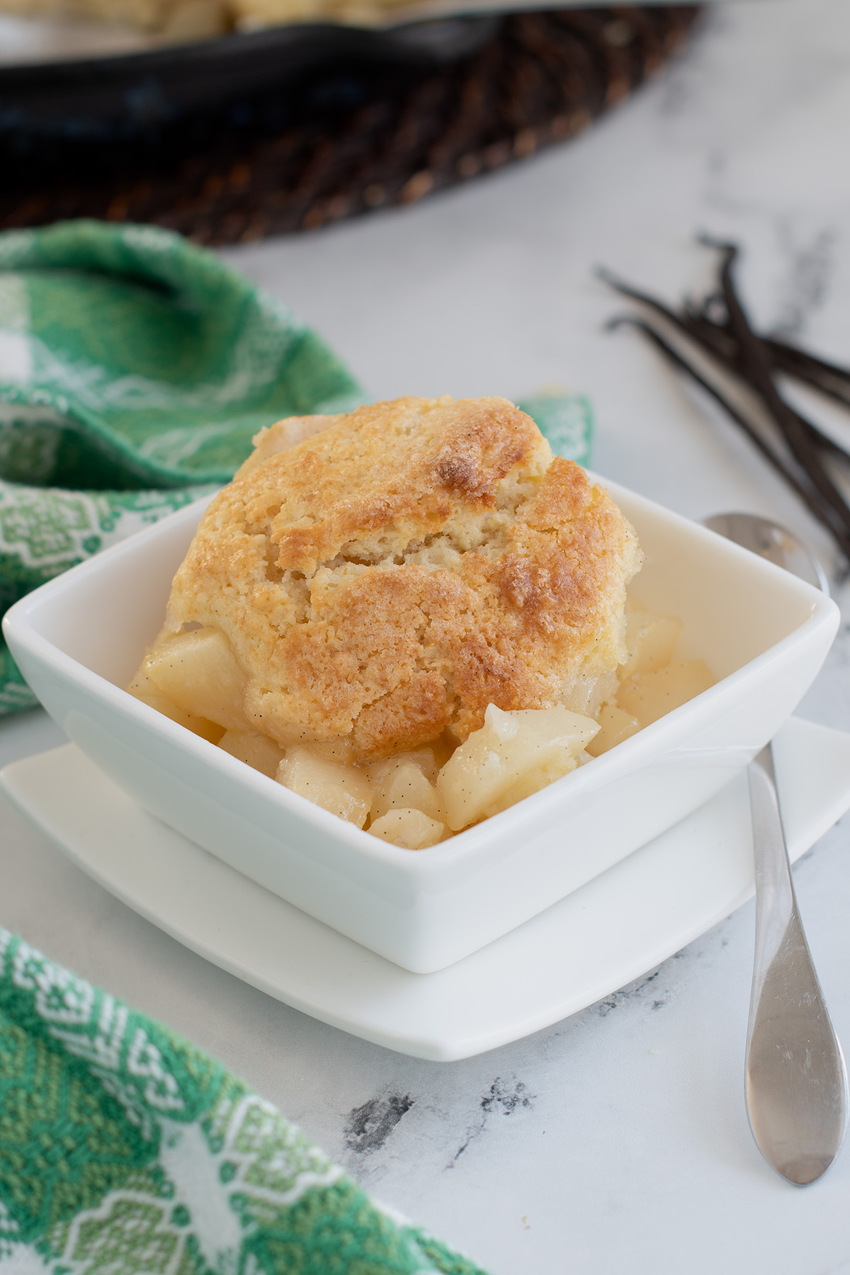 a pear cobbler in a white bowl next to a green towel.