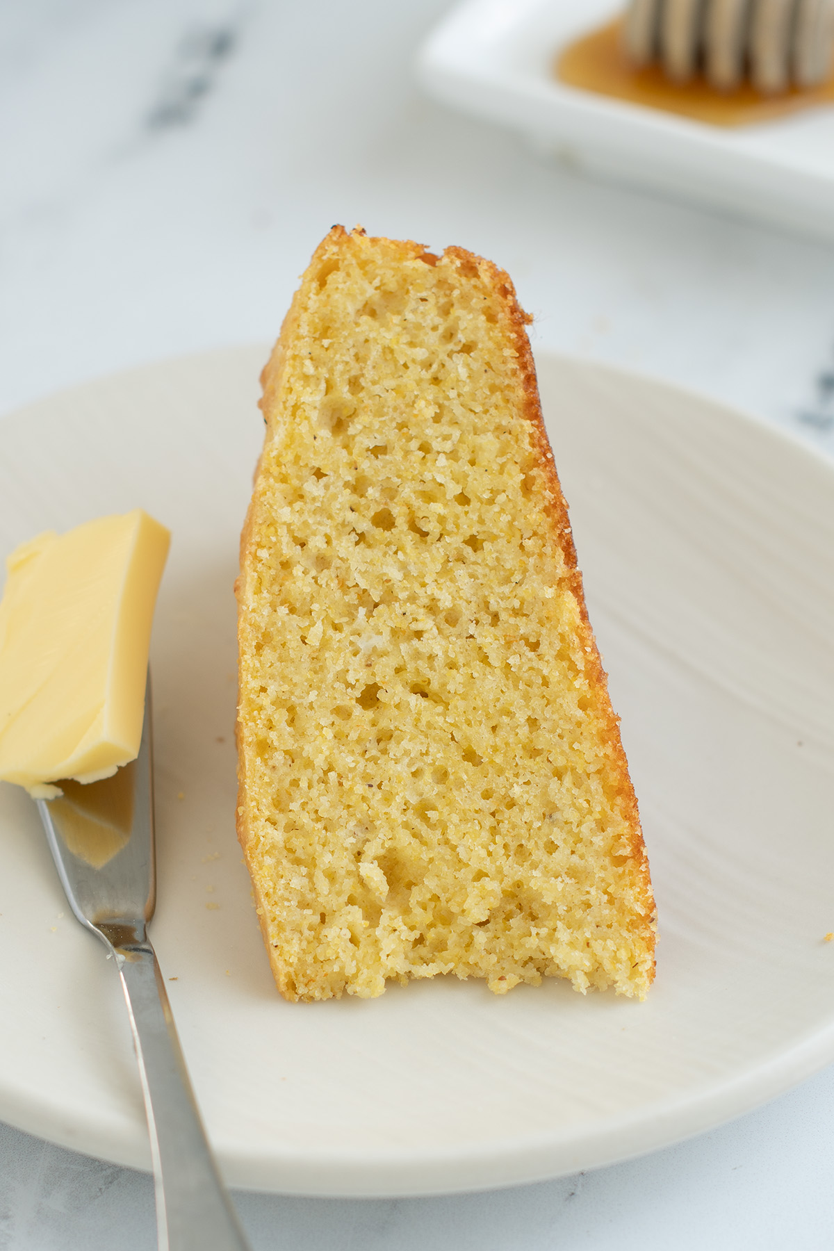 a slice of cornbread on a white plate with butter and knife.