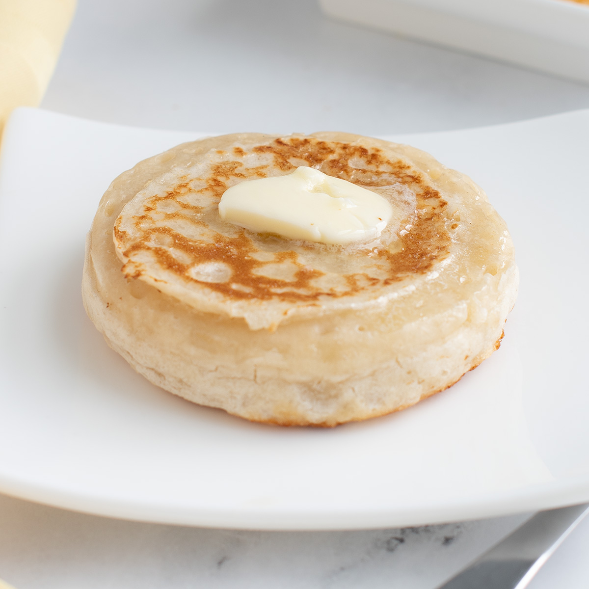 a buttered sourdough crumpet on a white plate.