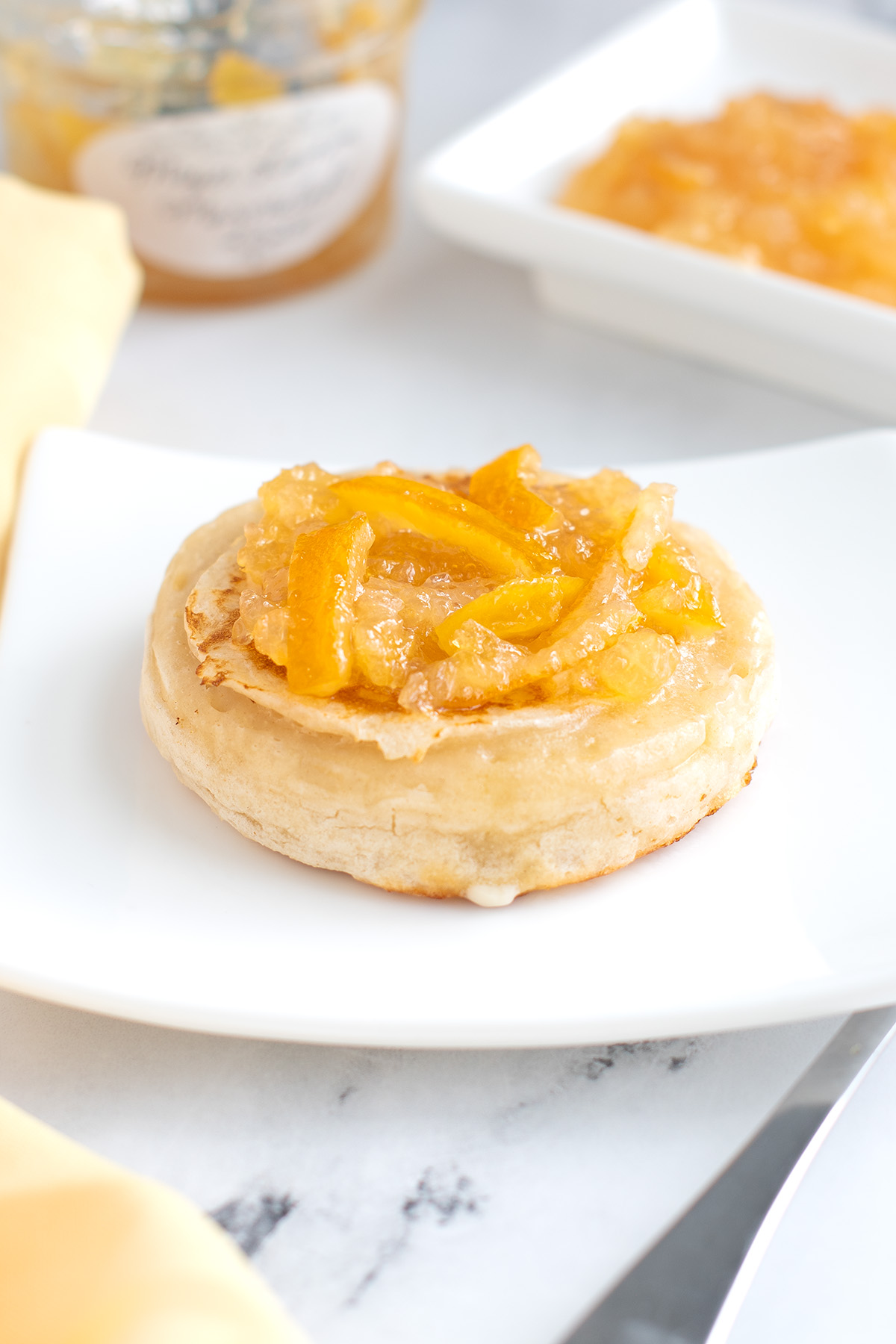 a sourdough crumpet topped with marmalade on a white plate.