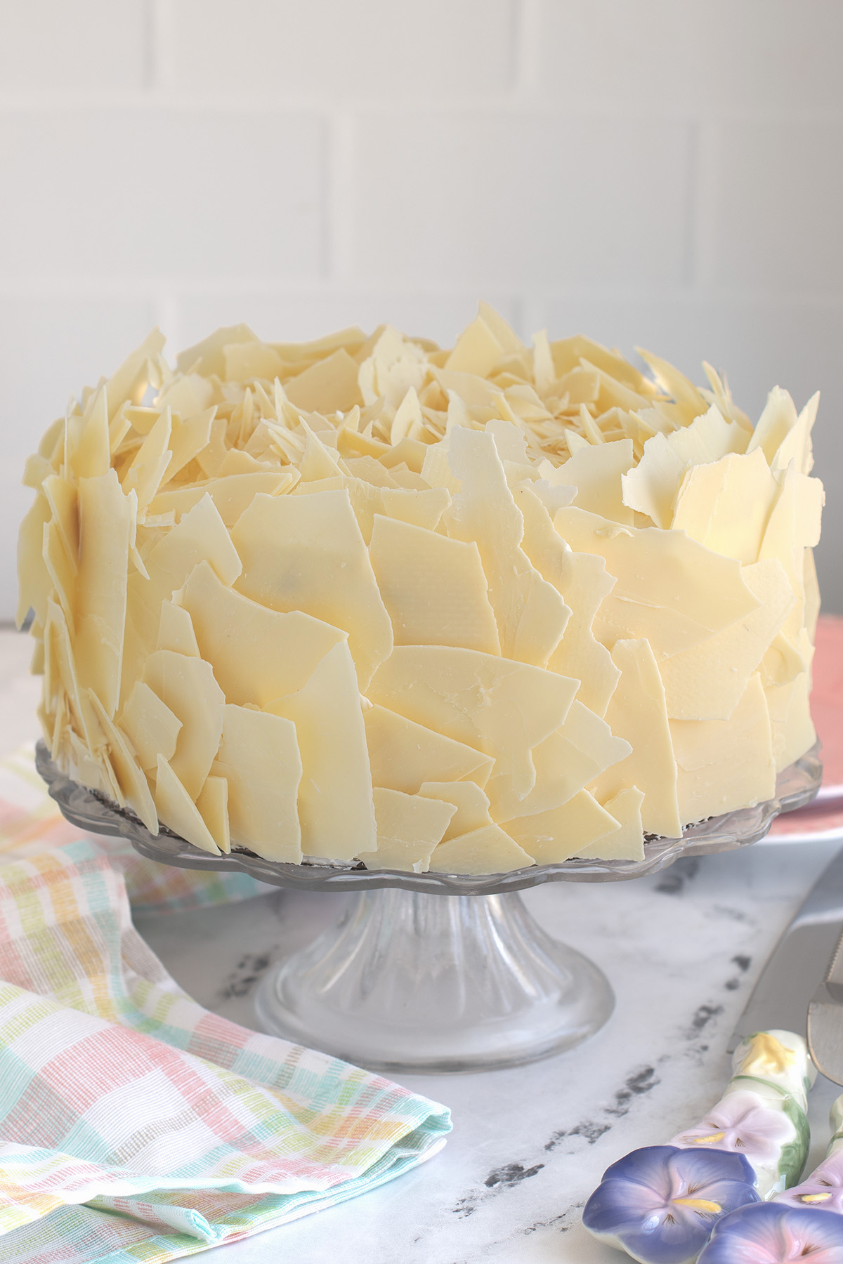 a cake covered with white chocolate flakes in a glass cake stand.