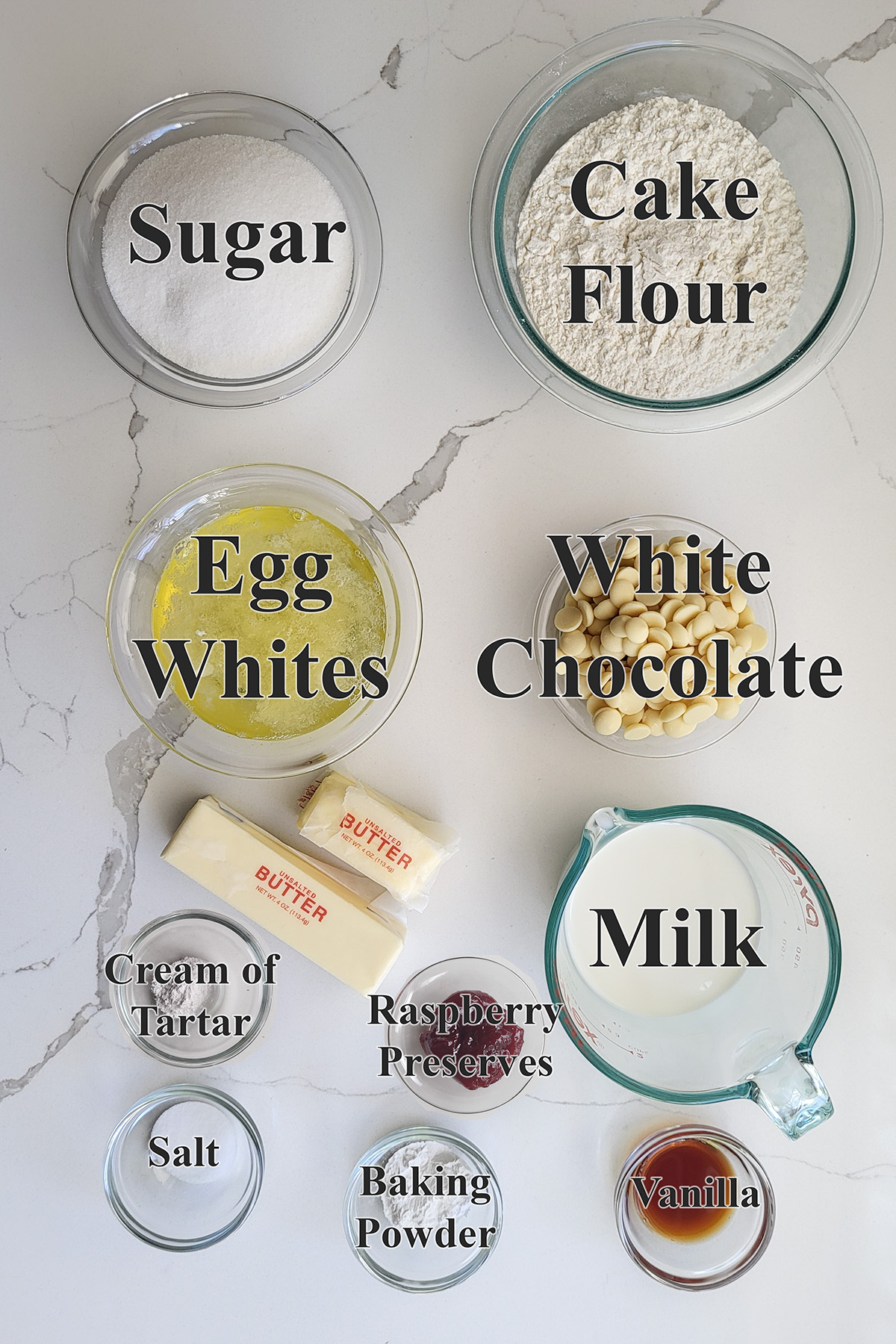 ingredients for white chocolate layer cake in glass bowls on a white surface.