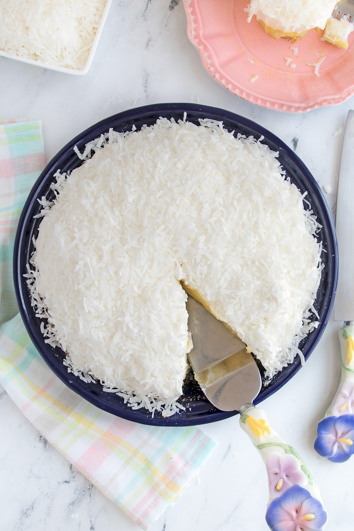 a coconut cream pie in a blue pie pan with a slice removed.