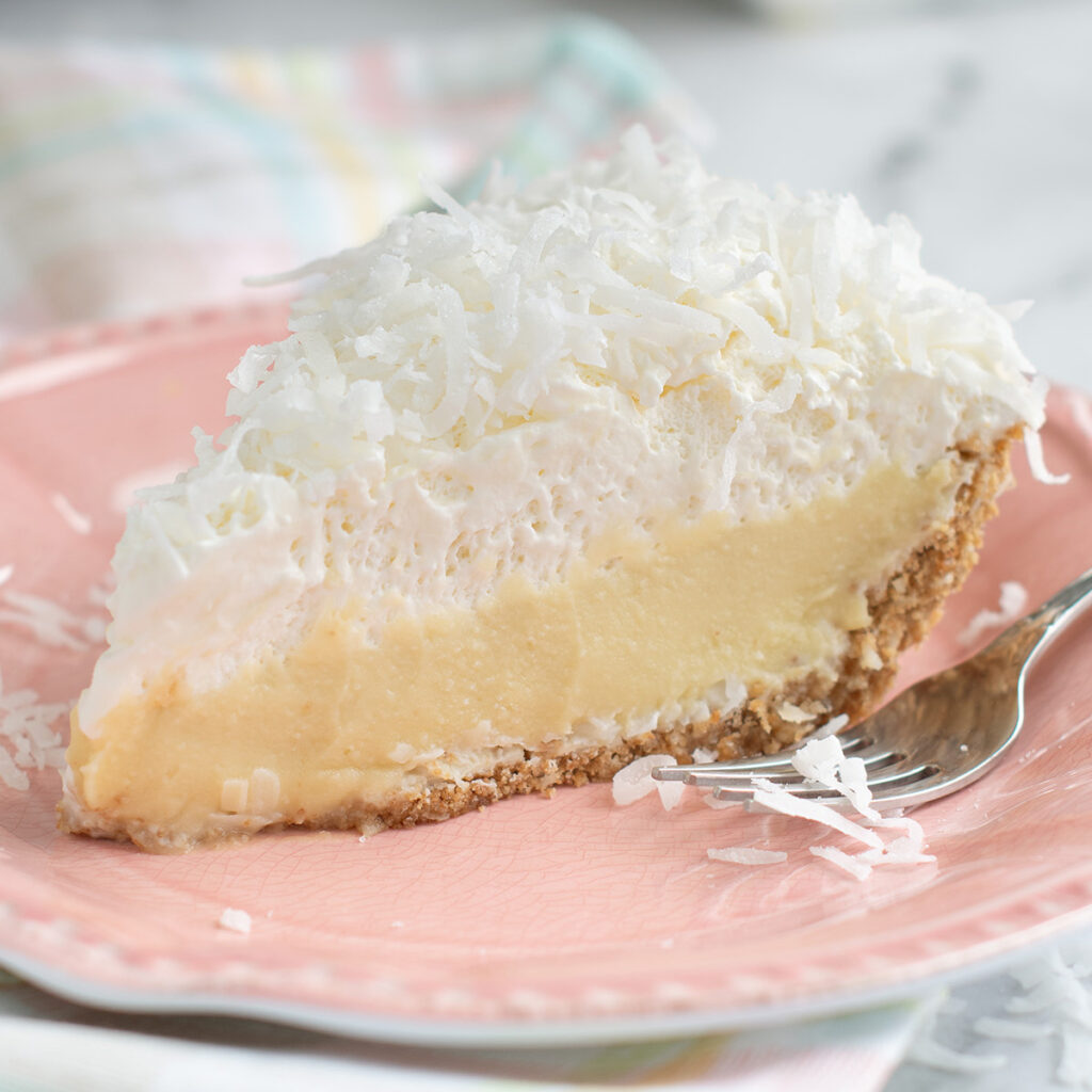 a slice of coconut cream pie on a pink plate with a fork.